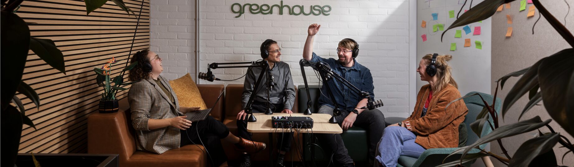Four people sit at a podcast set against a white wall