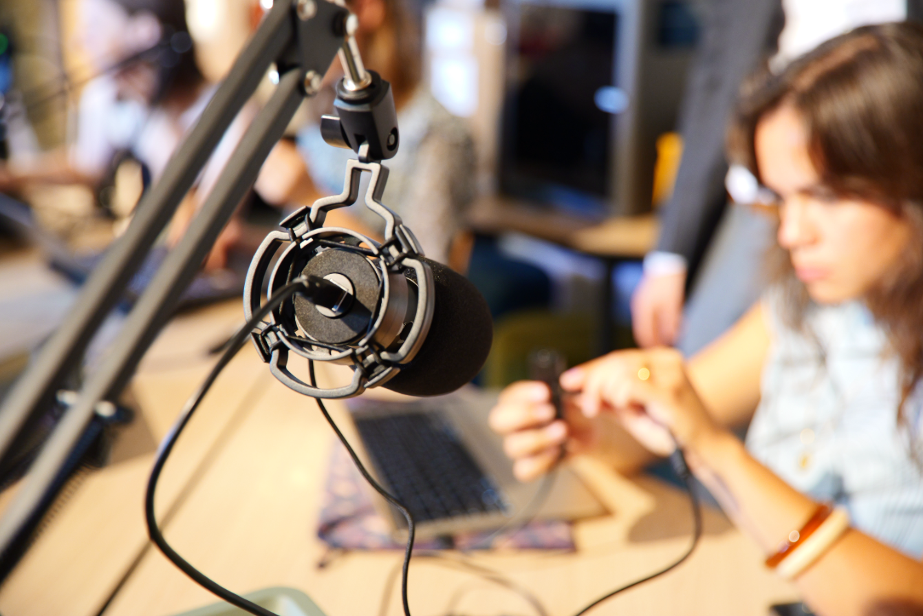 Photograph of a microphone in focus with a woman out of focus working on her computer