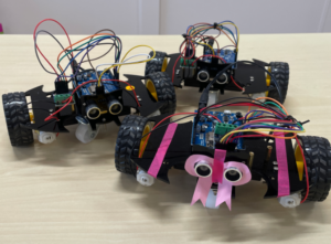 Photograph of 3 small robots on wheels with googly eyes on the front