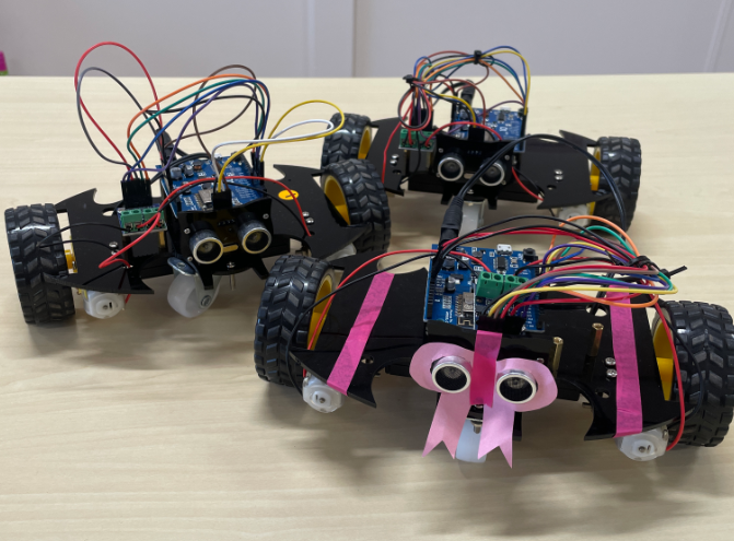 Photograph of 3 small robots on wheels with googly eyes on the front